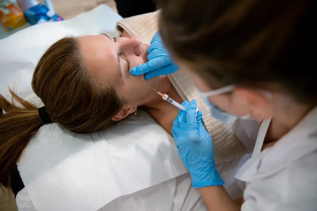 A woman receiving Xeomin injections in a clinical setting, administered by a medical professional wearing blue gloves—highlighting a common non-surgical facial rejuvenation treatment in Novi, MI.