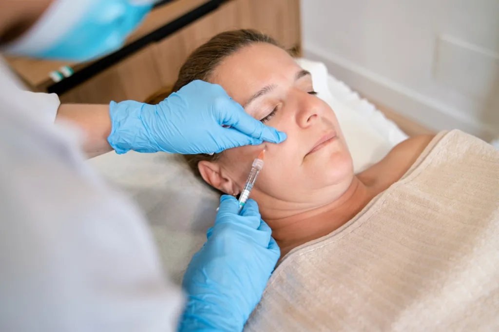 A healthcare provider wearing blue gloves administers a facial injection to a woman, showcasing one of the popular aesthetic treatments in Novi, Michigan.