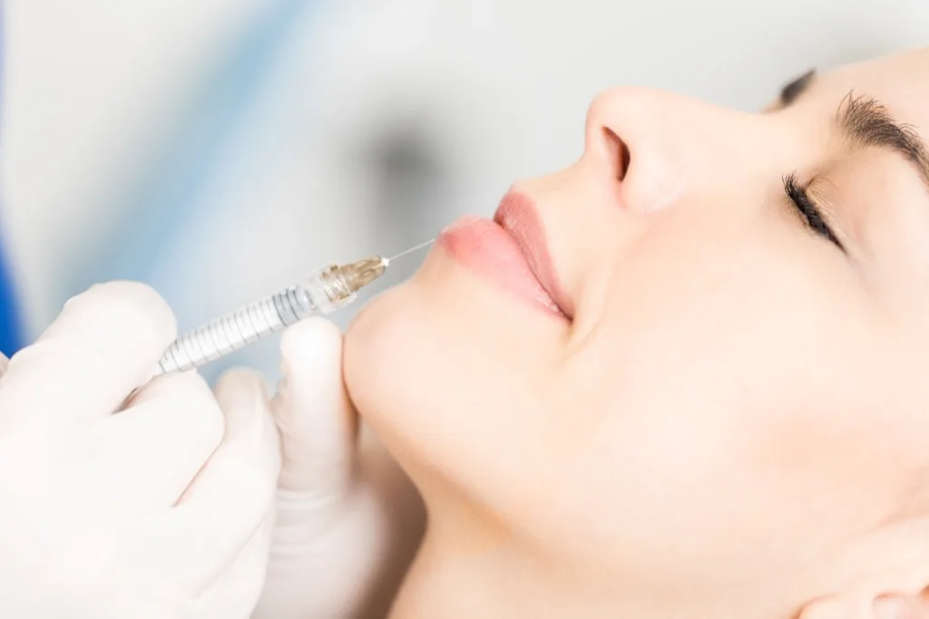 Woman receiving lip injection treatment with a syringe, representing affordable lip filler cost in Novi for fuller and natural-looking lips.