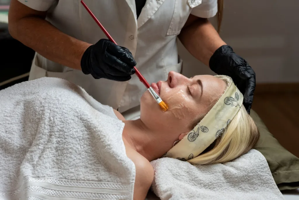 Client receiving a relaxing chemical peel in Novi as a skincare professional gently applies the solution with a brush during a spa treatment.
