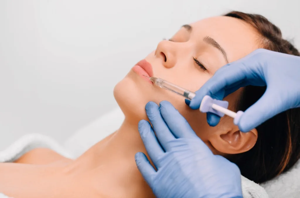 A woman receiving a Juvederm lip filler injection from a trained professional wearing blue medical gloves, enhancing her lips in a calm clinical setting.
